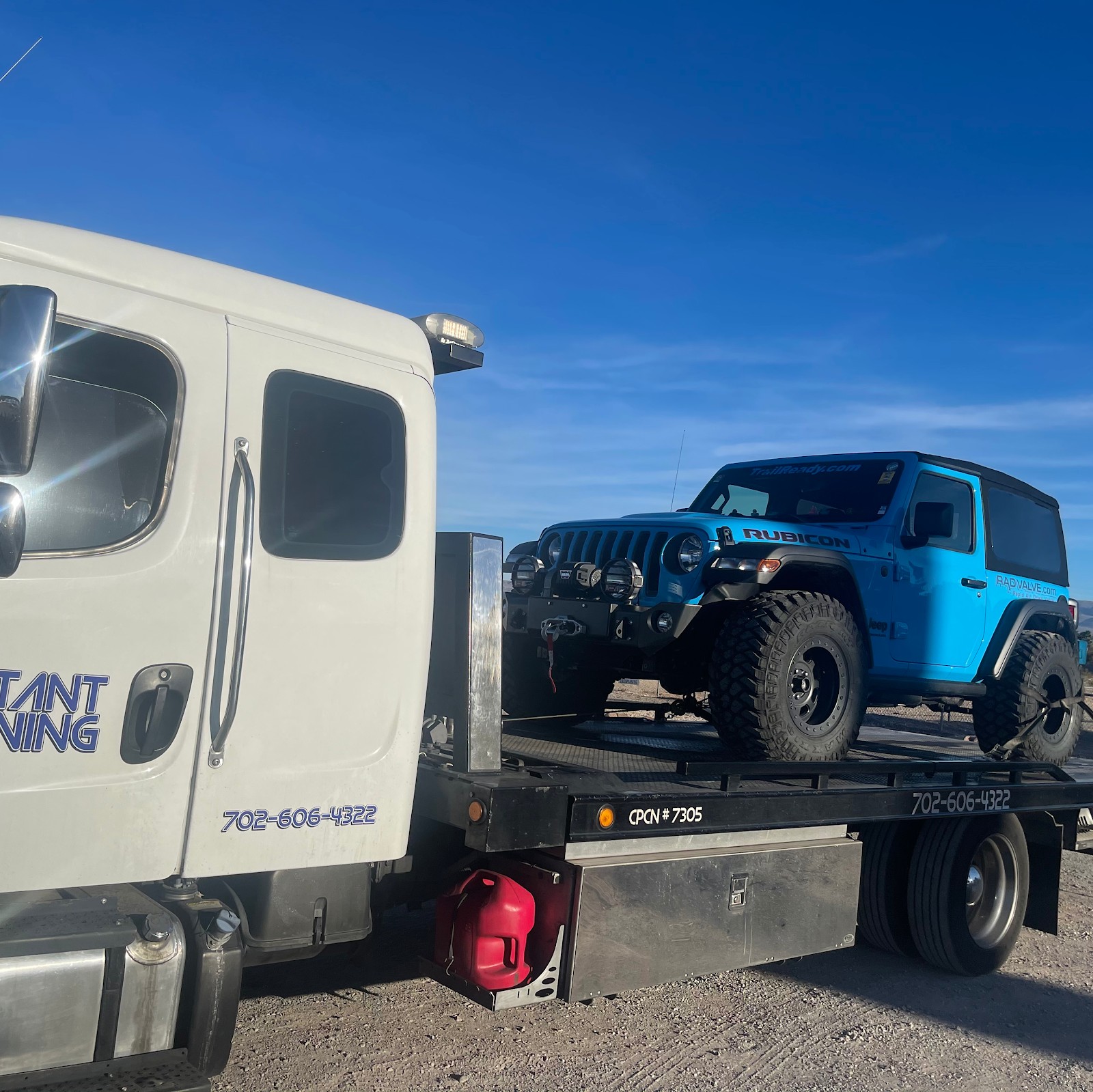 Instant Towing flatbed carrying a blue Jeep Wrangler Rubicon in the desert